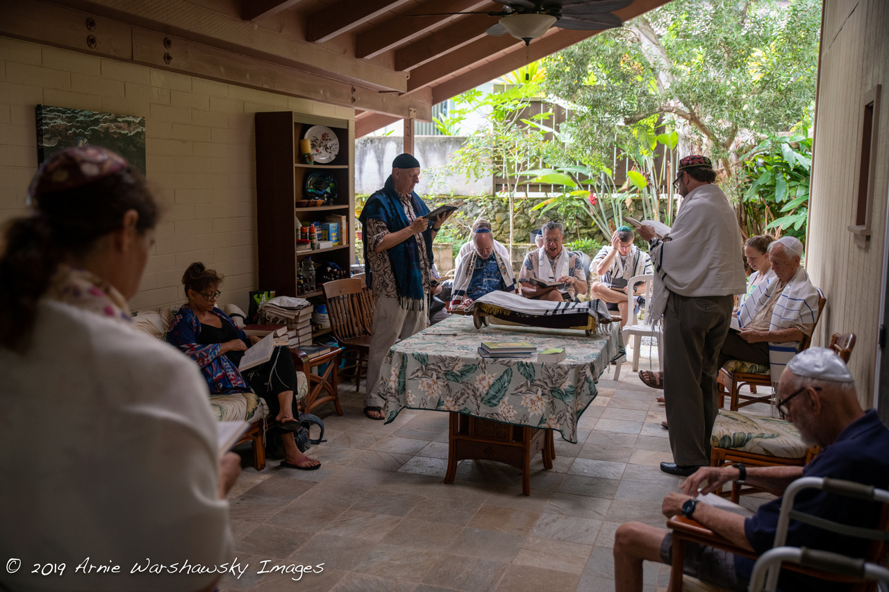 Several people on a lanai standing and sitting around a table with a torah scroll on it.